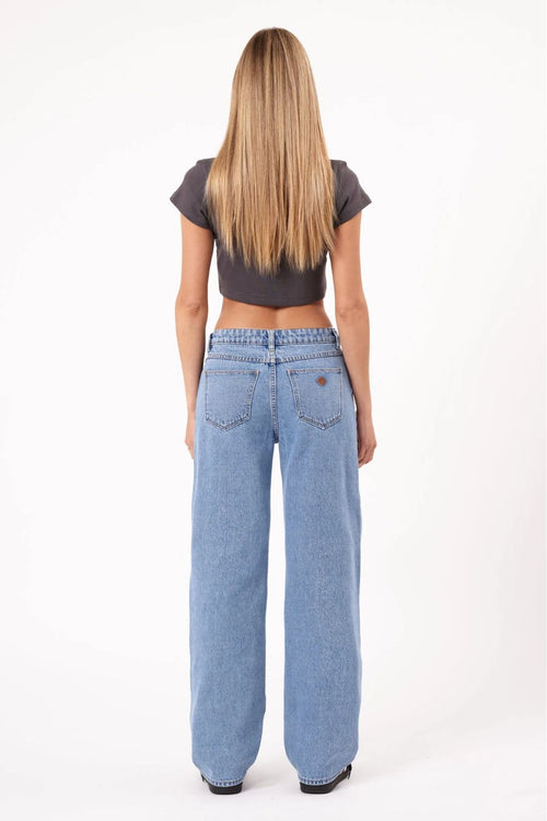 Person wearing a brown crop top and light blue jeans on a white background