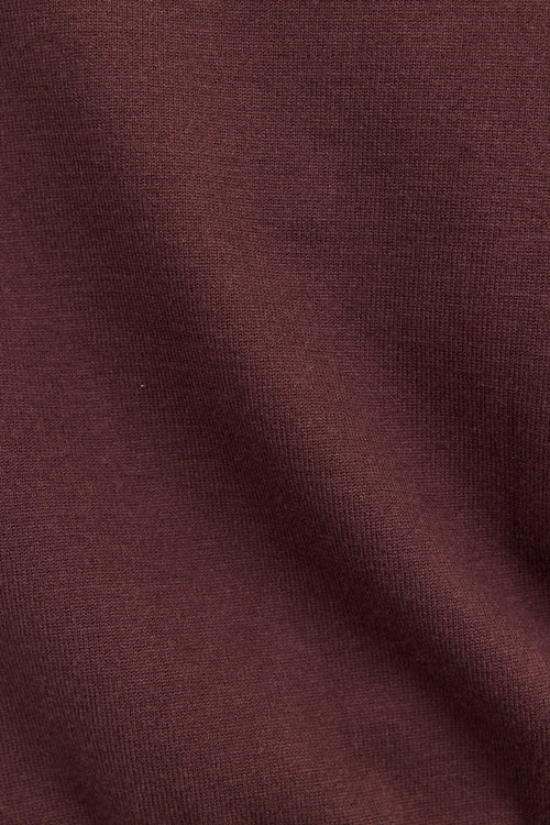 A close-up of a dark plum or burgundy knit fabric texture with soft folds.