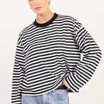 A woman modeling a black and white horizontally striped long-sleeve top with a black crew neck, paired with light-wash blue jeans, against a plain off-white background.