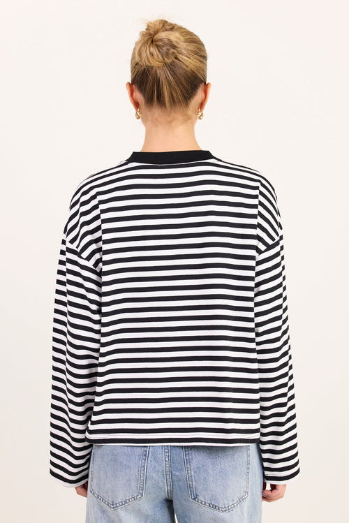 A person viewed from the back wearing a black and white horizontally striped long-sleeve top with a black crew neck, paired with light blue jeans, against a plain off-white background.