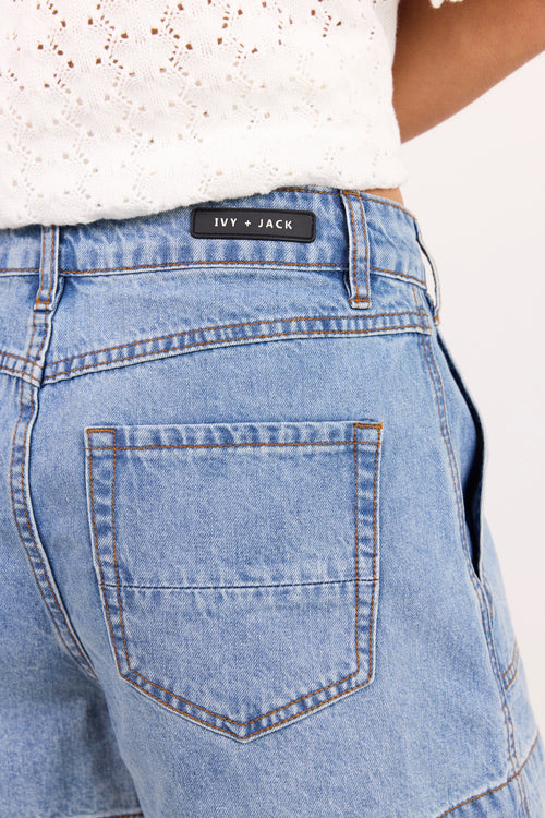 Close-up of the back waistband and pocket area of light blue denim jeans, showing a black brand label that reads 'IVY + JACK'.