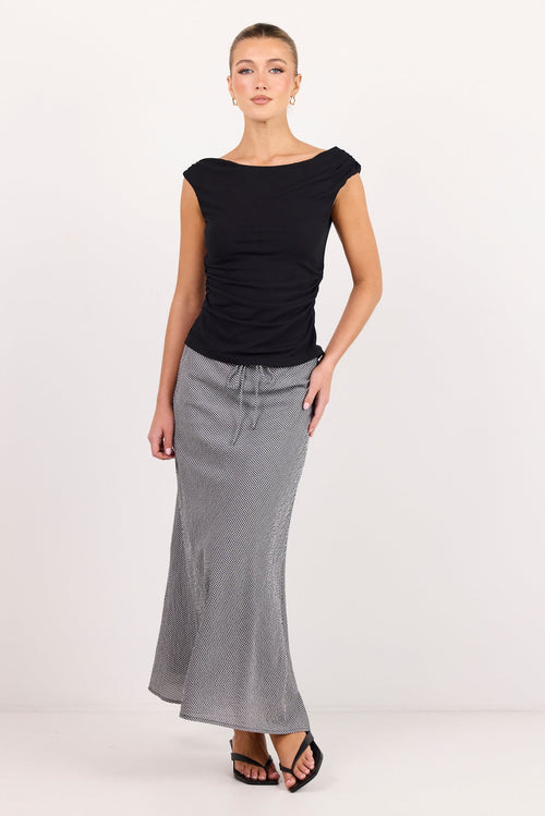 A woman modeling a black short-sleeve top and a long, flared gray skirt against a plain white studio background.