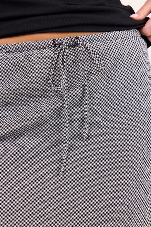 Close-up of a black and white gingham patterned skirt with a drawstring waistband, worn with a black top.