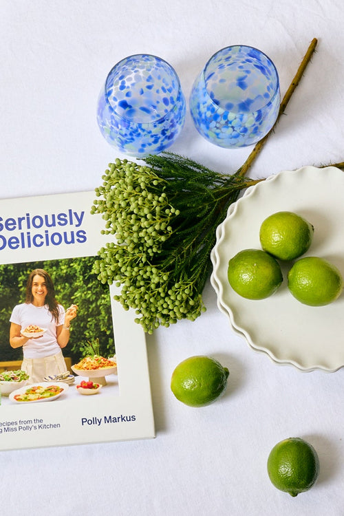 Round white table with decorative items including a book, flowers, and limes on a light-colored floor.