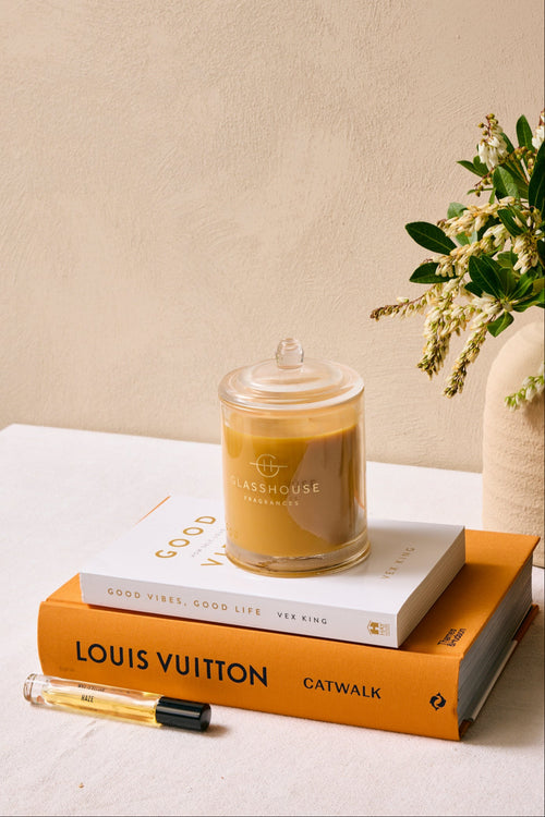 Candle, books, and a vase with flowers on a surface against a beige wall.