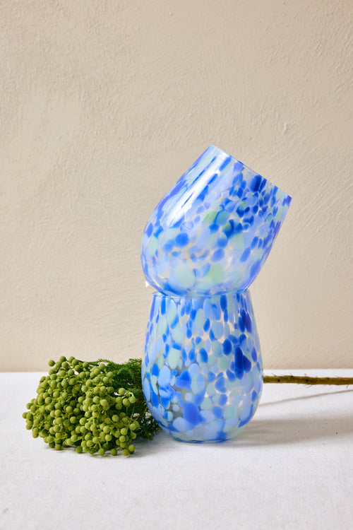 Blue and white speckled glass vase on a white surface with a beige background
