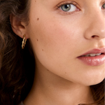 Close-up of a woman wearing gold hoop earrings with a neutral background