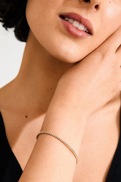 Close-up of a woman wearing a delicate gold bracelet on a plain background