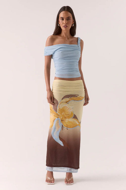 Woman wearing a light blue off-shoulder top and a long, patterned skirt on a white background