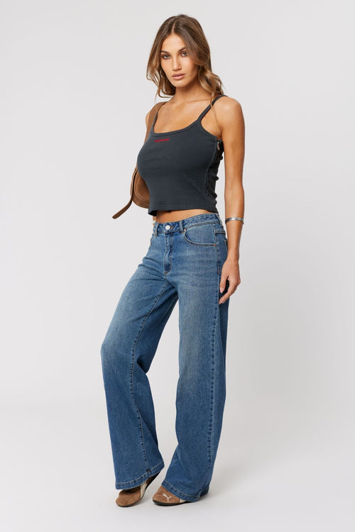 Woman wearing a black tank top and blue jeans on a white background