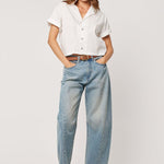 Woman wearing a white top with light wash blue barrel jeans 