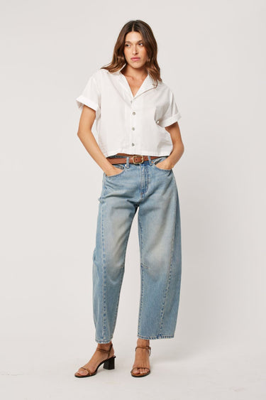 Woman wearing a white top with light wash blue barrel jeans 