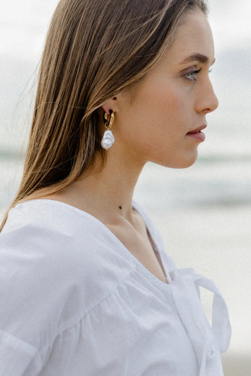 A pair of gold-toned hoop earrings featuring dangling baroque freshwater pearls, suspended from smooth, polished hoops for an elegant and organic look