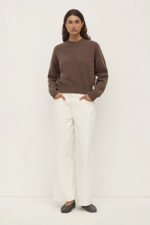 Person wearing a brown sweater and white pants on a white background