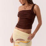 Woman wearing a brown one-shoulder top and a yellow skirt with a floral design on a white background