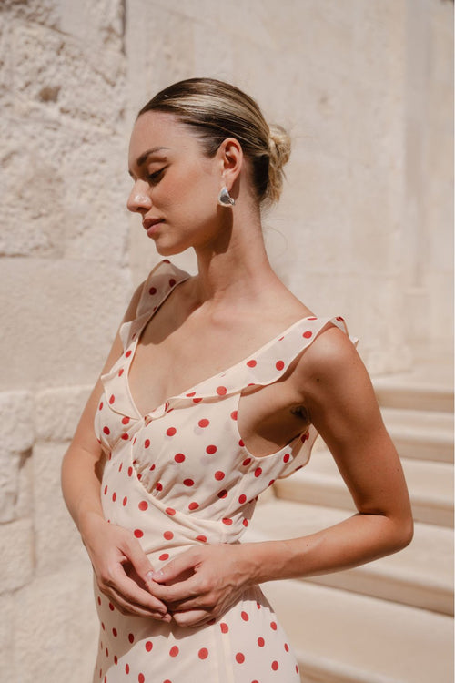 Woman wearing a cream and red polka dot slip maxi dress with adjustable straps, V-neckline, and a flowing bias-cut design.