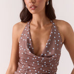 Woman wearing a ruched halter neck top in brown and blue polka dots with the matching skirt