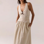 Woman wearing a beige halter neck dress against a plain background