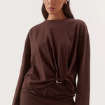 A woman modeling a dark brown long-sleeve top and matching mini skirt set against a plain light background.