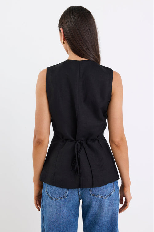 Person wearing a black sleeveless top with a tie waist and blue jeans on a white background