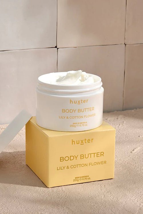 An open white jar of Huxter body butter in the scent 