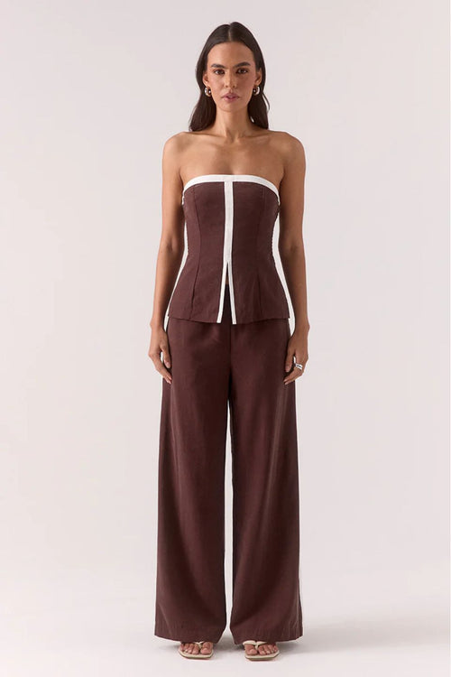 Woman wearing a brown strapless top and wide-leg pants on a white background