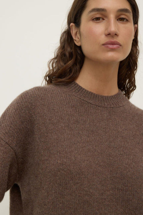 Woman wearing a brown sweater against a plain background