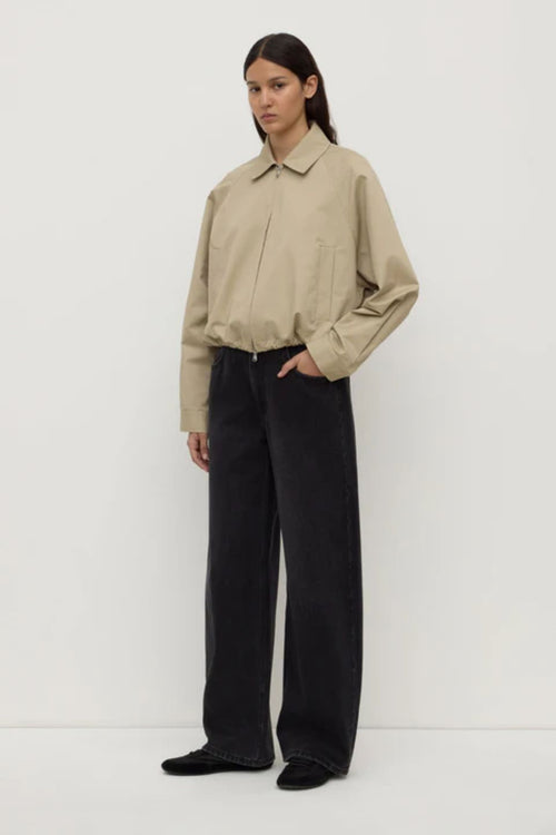 Person wearing a beige jacket and black pants on a white background