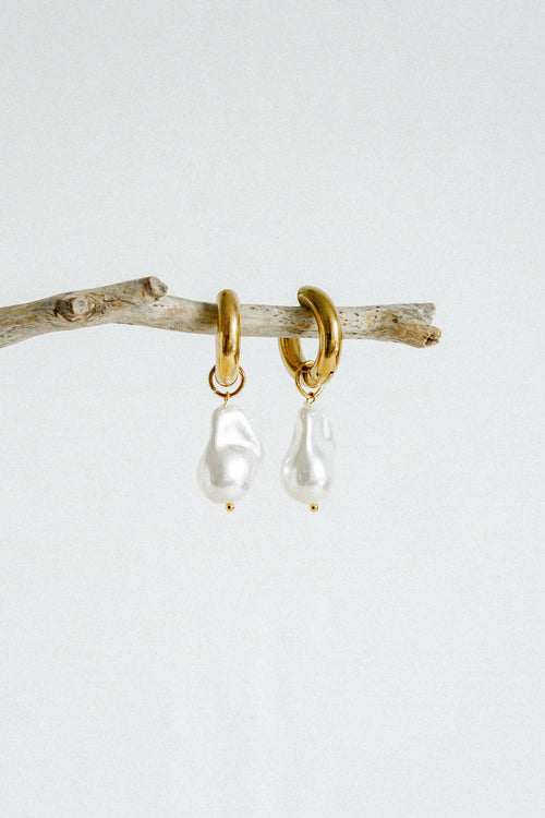 A pair of gold-toned hoop earrings featuring dangling baroque freshwater pearls, suspended from smooth, polished hoops for an elegant and organic look