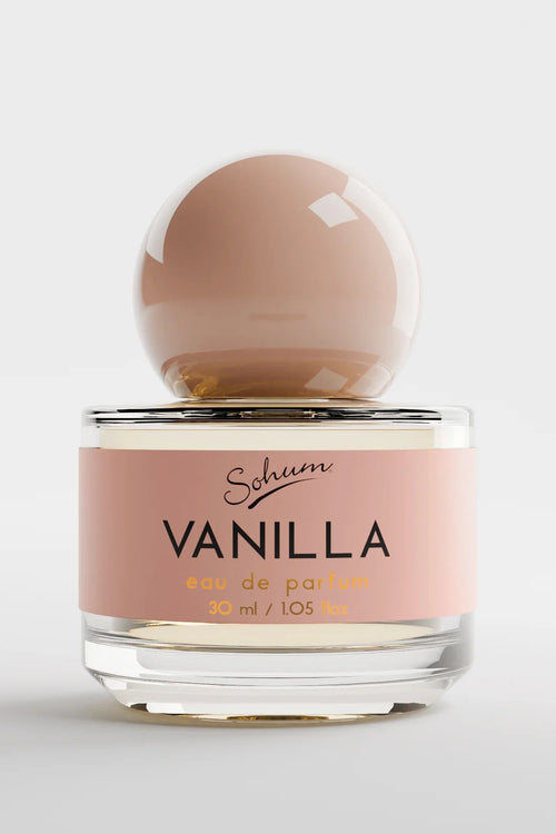 A round glass bottle of Sohum Vanilla eau de parfum with a glossy blush-toned spherical cap and a warm beige-pink label, featuring bold black and soft golden text for a cosy, elegant appearance.