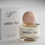 A round glass bottle of Sohum Green Tea eau de parfum with a soft blush-toned spherical lid, placed beside its minimal white textured box. The label is cream with black and amber lettering.
