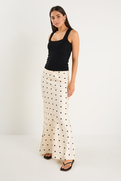 the model wears a cream maxi skirt with black polka dots and a black tank top