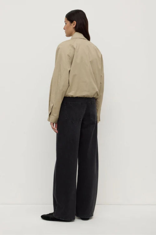 Person wearing a beige jacket and black pants on a white background