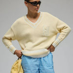 Person wearing a light yellow sweater, blue checkered shorts, and white sneakers on a gray background