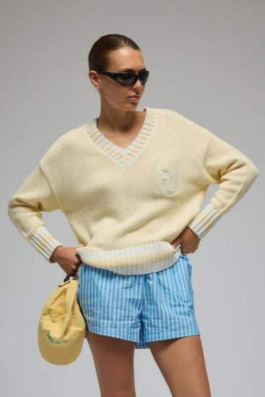Person wearing a light yellow sweater, blue checkered shorts, and white sneakers on a gray background
