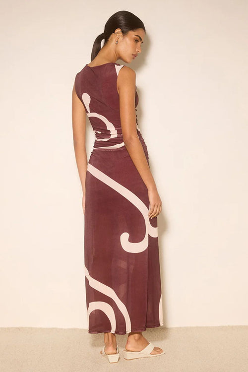 Woman wearing a long burgundy dress with white patterns against a beige background