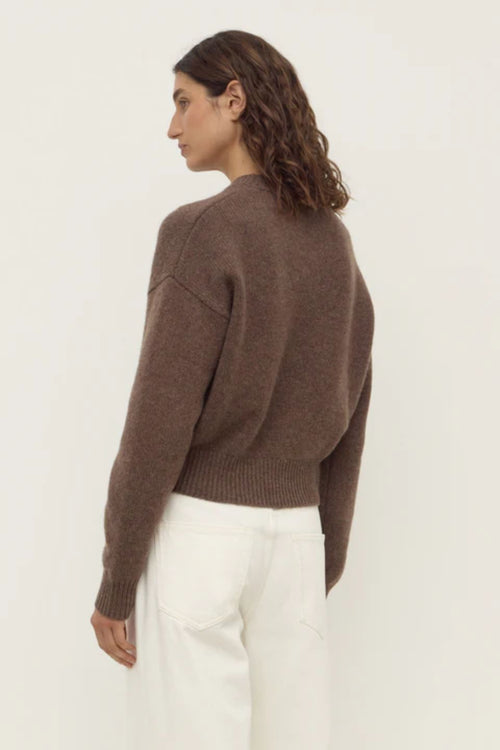 Person wearing a brown sweater and white pants on a plain background
