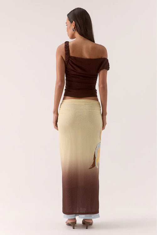 Woman wearing a one-shoulder brown top and a long, gradient skirt on a white background