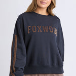 Woman wearing a navy sweatshirt with 'FOXWOOD' text on a light gray background