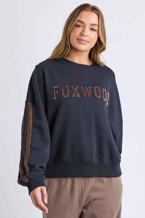 Woman wearing a navy sweatshirt with 'FOXWOOD' text on a light gray background