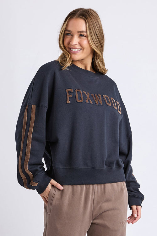 Woman wearing a navy sweatshirt with 'FOXWOOD' text and brown pants on a white background