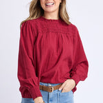 Woman wearing a red blouse and light blue jeans on a white background