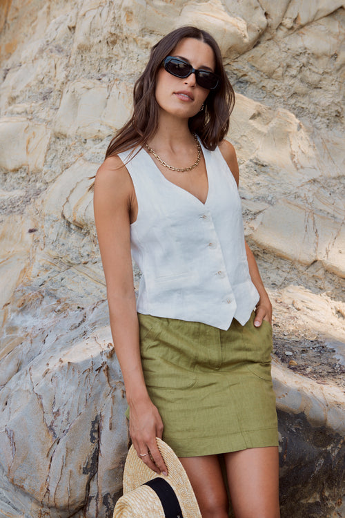 model wears linen vest and green linen mini skirt at the beach