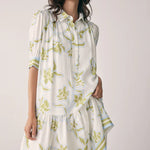 Woman wearing a white dress with green floral pattern against a plain background