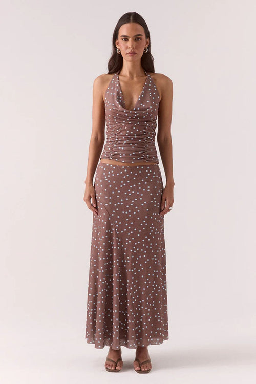 Woman wearing a ruched halter neck top in brown and blue polka dots with the matching skirt