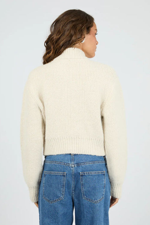 Person wearing a cream sweater and blue jeans on a light gray background