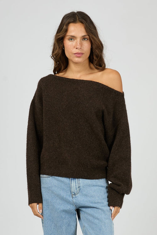 Woman wearing a brown off-shoulder sweater and light blue jeans on a white background