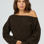 Woman wearing a brown off-shoulder sweater and light blue jeans on a white background