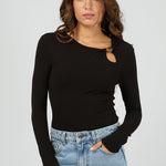 Woman wearing a black long-sleeve top with a cutout design and light blue jeans on a gray background