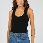 A woman modeling a black scoop-neck tank top paired with blue jeans against a light gray studio background.
